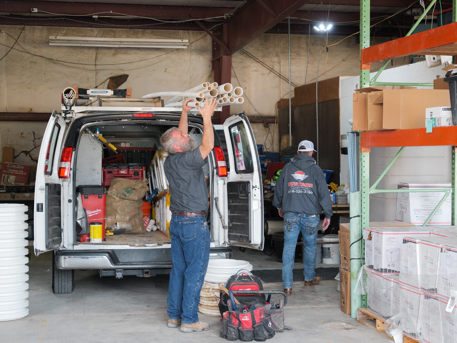 A man stands on the back of a van, looking out over the surroundings with a focused expression.